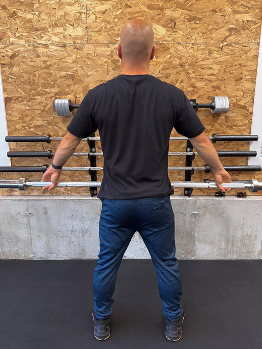 Man standing in front of a wall with barbell racks in a gym setting wearing navy Sweat Storm Apparel joggers and black pain is temporary t-shirt