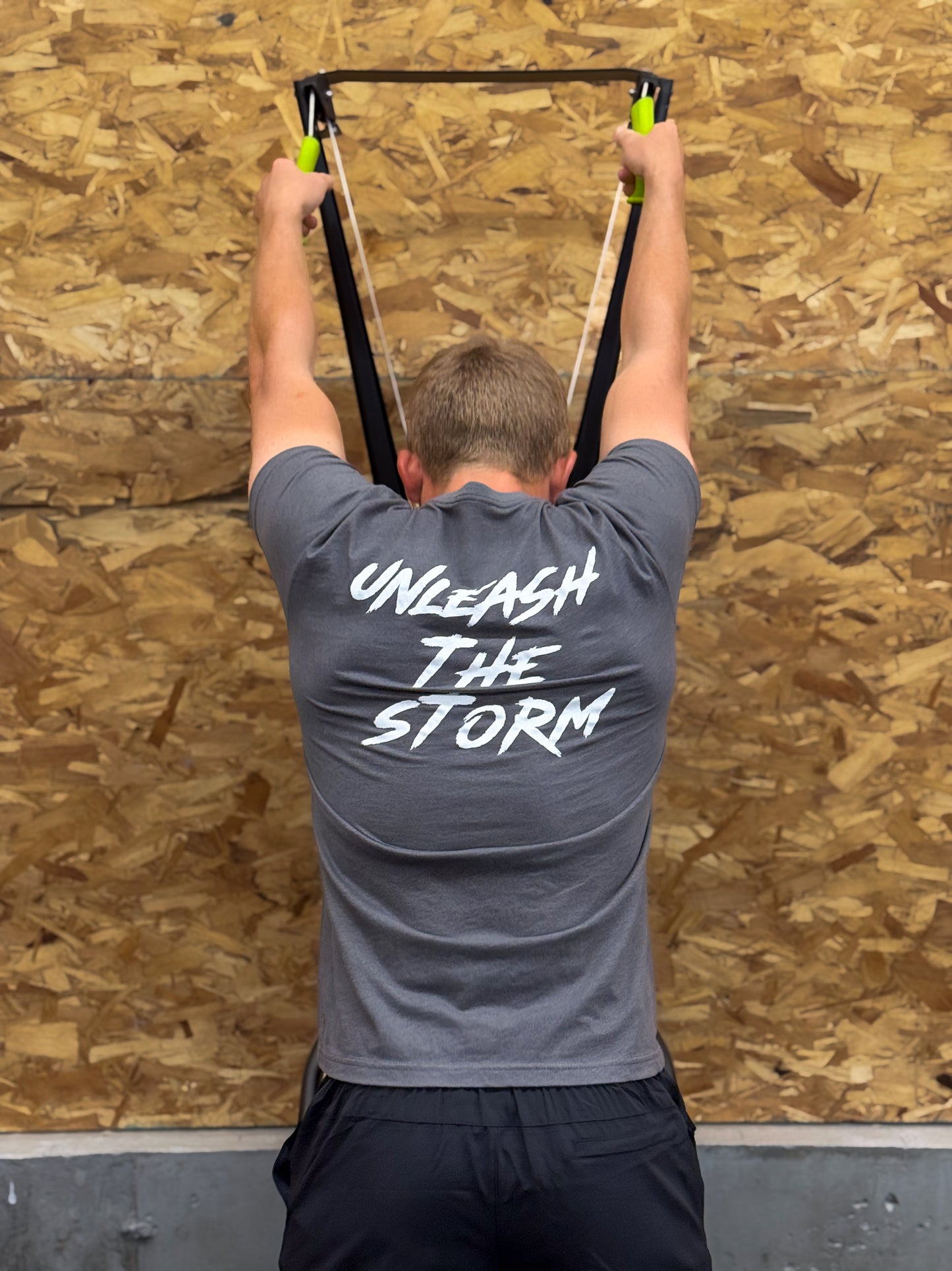 Person using ski machine against a wooden wall with 'Unleash The Storm' text on shirt.
