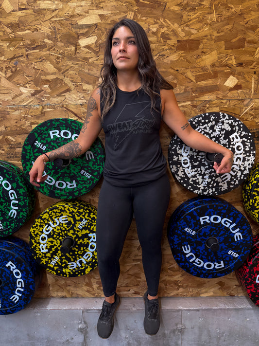 Woman posing with Rogue weight plates against a wooden wall in black Sweat Storm Apparel tank top