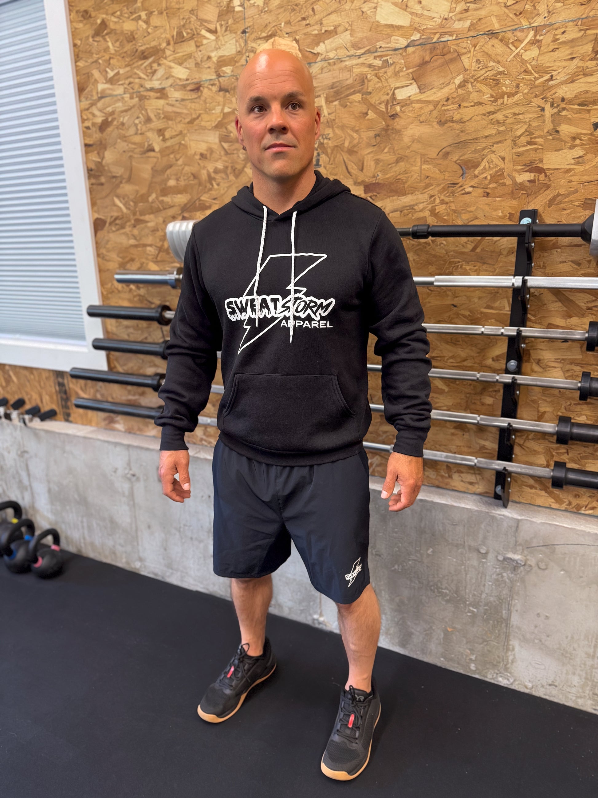 Man wearing a black hoodie with a Sweat Storm Apparel logo in a gym setting