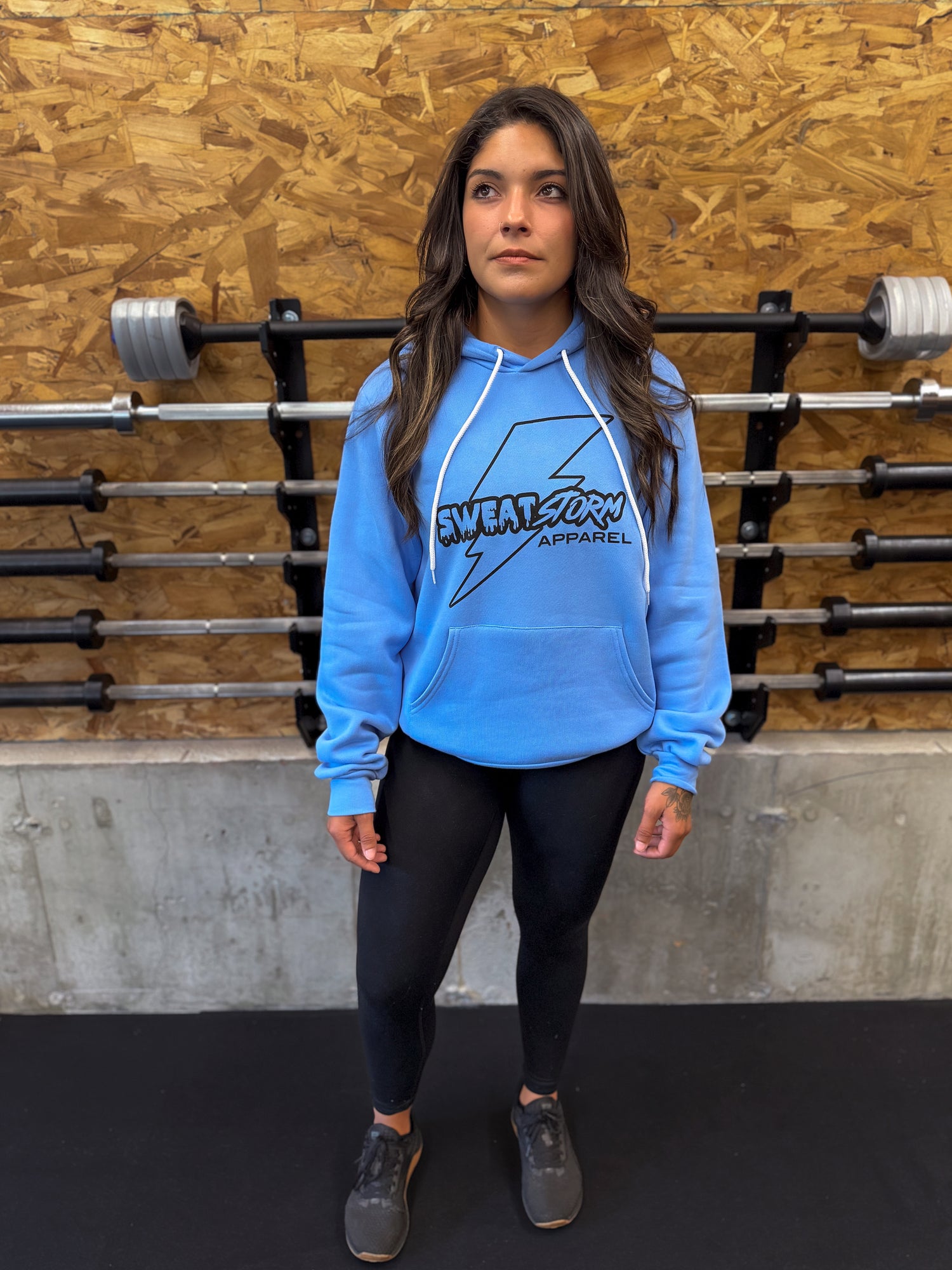 Person wearing a blue hoodie with a logo in front of gym equipment.